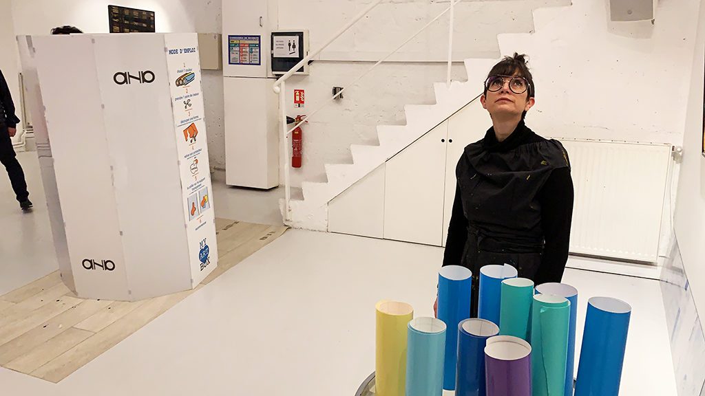 avant une séance de live painting, une femme debout derrière son matériel et devant son support artistique dans un loft tout blanc