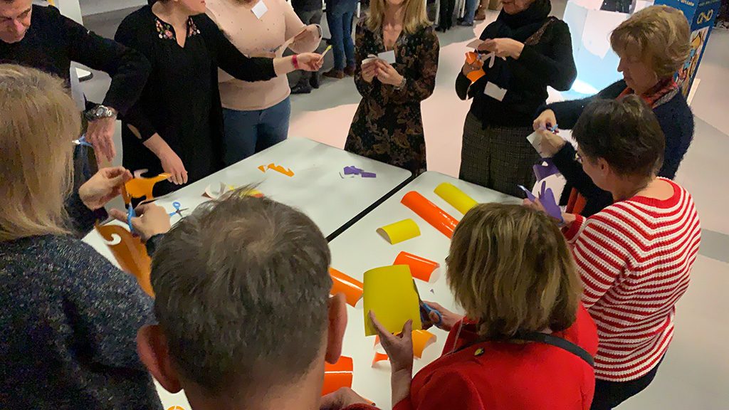 Atelier team building créatif d'un groupe de collaborateurs rassemblés autour d'une table de travail et en train de découper des formes colorées dans des adhésifs à poser sur le tube fresque plexi art de l'artiste aNa pour my art box à Lyon