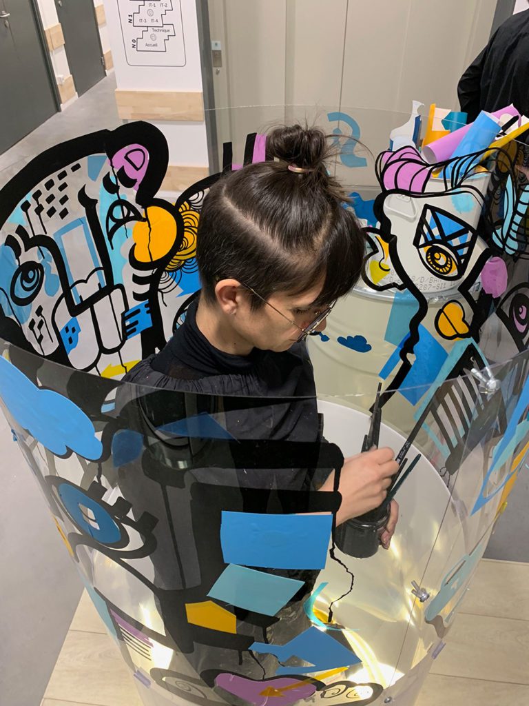 une artiste dans un tube transparent en live painting lors du salon préventica