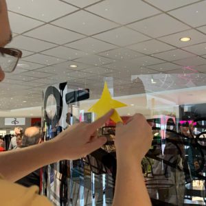 Une personne colle une étoile jaune sur un tube plexi géant en animation fresque adhésive Totem Box