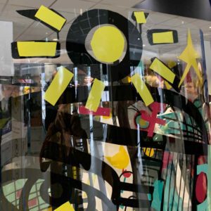 Un symbole de soleil jaune découpé dans du vinyle de couleur et posé sur le Tube plexi Totem Box Animation Fresque My Art Box