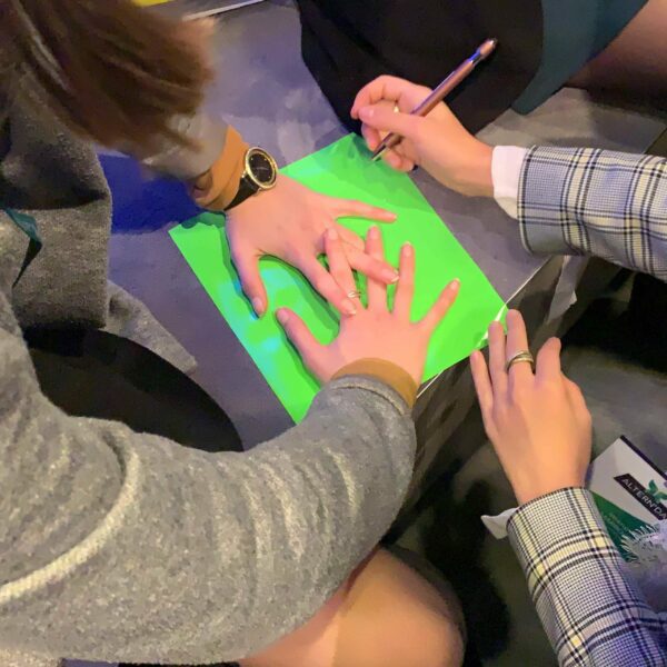 Des jeunes femme en gros plan sur leurs mains en train de découper le contour de leurs doigts pour représenter l'idée animation cohésion lors d'une animation fresque my art box format Totem Box XL