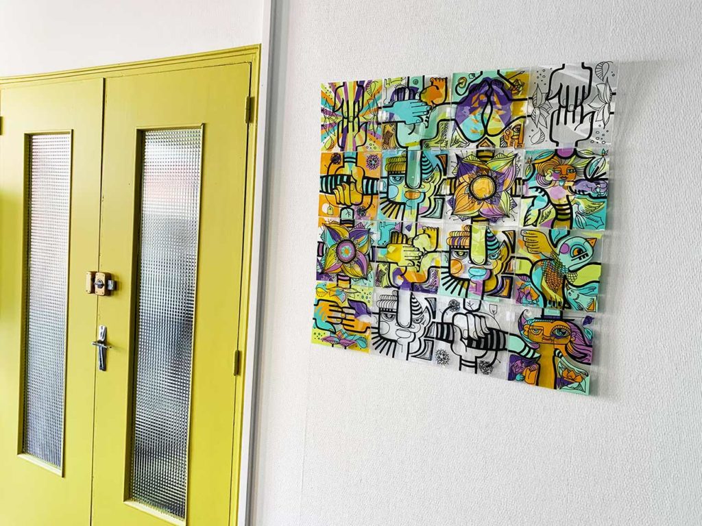 création en confinement sous forme d'un tableau coloré accroché au mur à coté d'une double porte verte dans une entreprise