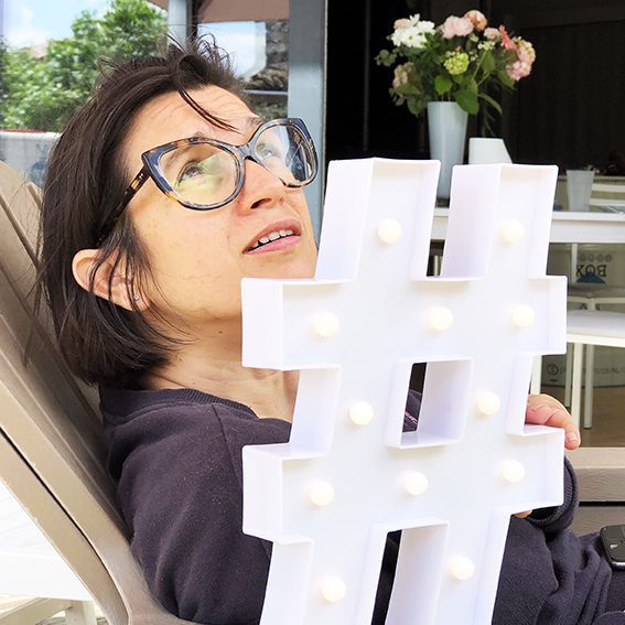 aNa artiste pose derrière un Hashtag lumineux blanc pour présenter son service de puzzle décoratif qui aide à développer son business avec instagram