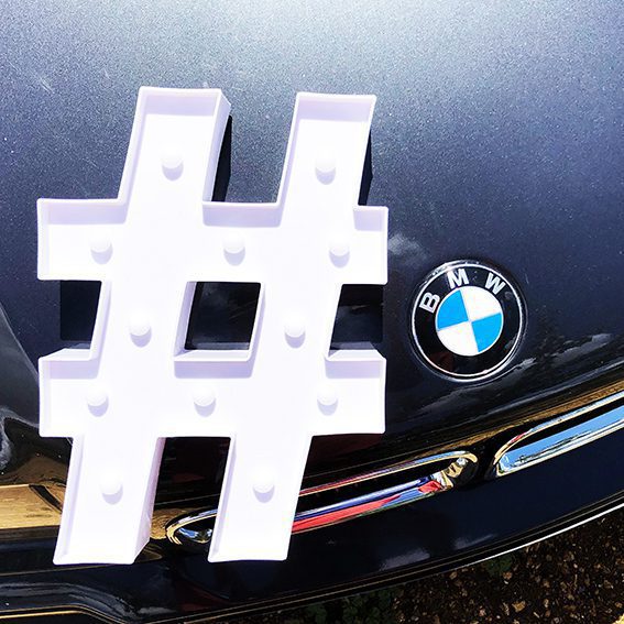 sur une bmw m3 e36 noir un hashtag blanc design posé à coté du logo de la marque BMW pour illustrer comment développer son business avec instagram