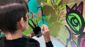 aNa artiste en train de peindre une fresque dans son cylindre transparente en plexiglas lors d'un team building blogueuses à Reims et aussi disponible dans toute la France au même prix