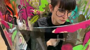 aNa artiste de fresque collective à Reims en train de peindre dans son tube en plexiglas lors d'un team building blogueuses my-art-box.com