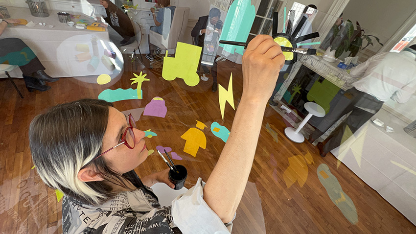 1 fresque Live en team building pour avocats à 50 à Paris 15 ana artiste peint dans son tube plexi transparent en team-building pour avocats éco-responsable et sobre à Paris animé par Christophe Chazot