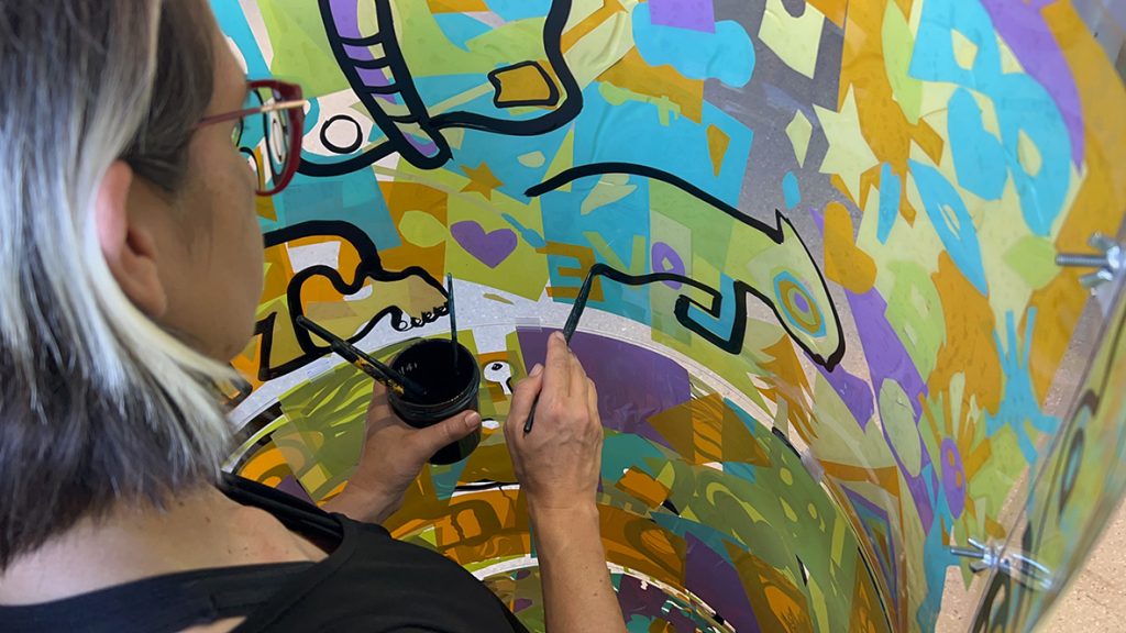 ana artiste en train de peindre une silhouette d'animal dans son cylindre en plexi recyclable en animation fresque éco-responsable à Genève animée par Christophe Chazot