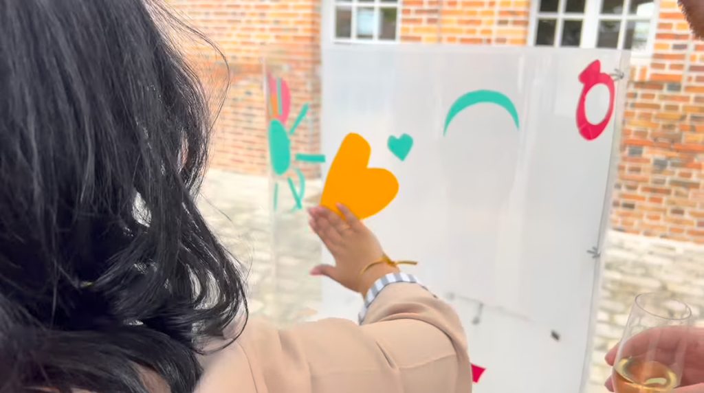 Une participante l'animation fresque pour mariage à Orleans colle un sticker découpé en forme de coeur orange sur le plexiglas de aNa artiste