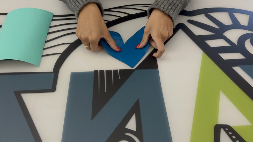 Un coeur bleu découpé dans du vinyle pour la fresque logo éco-responsable par une participante qui le colle sur le plexi