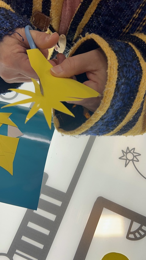 Un symbole de soleil en vinyle jaune en train d'être découpé par une participante pour coller sur la fresque zen de Cluny animée par Christophe Chazot