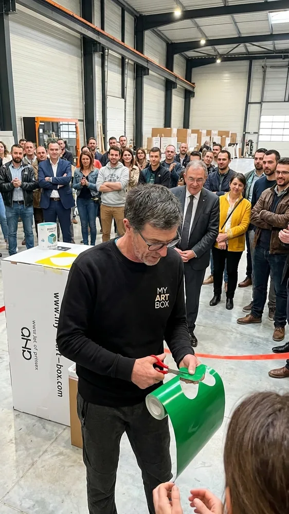 Animateur en vêtements My Art Box montrant la découpe d'un coeur vert en vinyle lors de l'inauguration artistique à Fruges, fresque collaborative, événement écologique