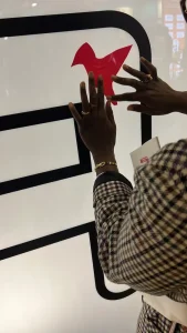 Participante contribuant à une sculpture collaborative en plexiglas sur un stand lors d’un salon ou d’une convention (format 200–400 personnes)