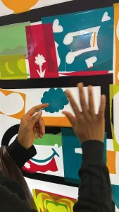 Main d’un participant ajoutant une forme colorée sur une sculpture collaborative en plexiglas lors de l’animation CUBE My Art Box (200 à 400 personnes).