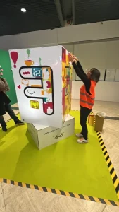 Sculpture collaborative en plexiglas en format totem installée dans un hall, avec motifs colorés réalisés par 200 à 400 participants