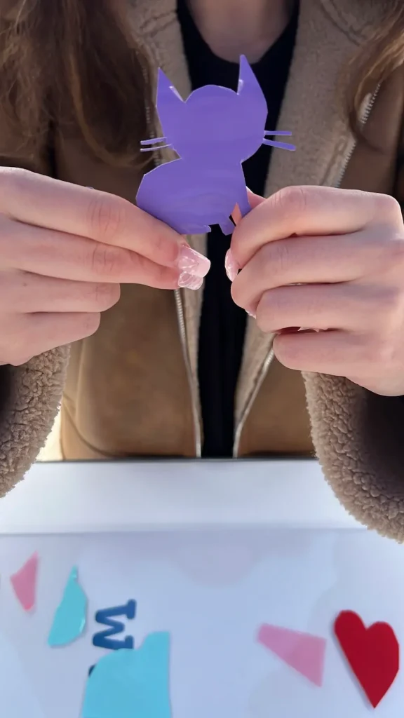 Participante tenant une forme de chat en vinyle violet découpée pour une fresque collaborative éco-responsable