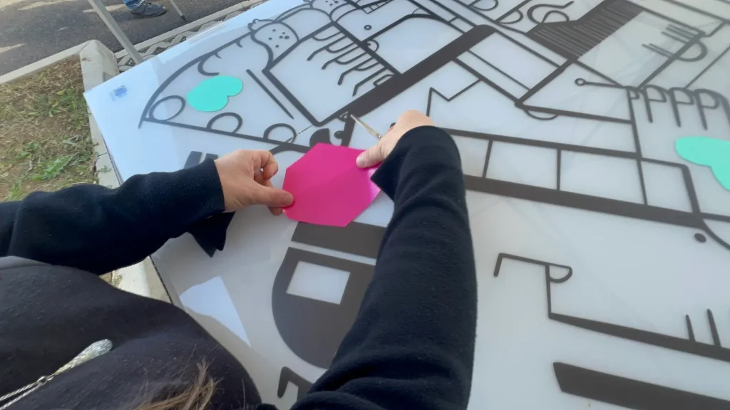 Main d’un participant posant une forme adhésive colorée sur une fresque en plexiglas basée sur un plan immobilier lors d’une animation RSE
