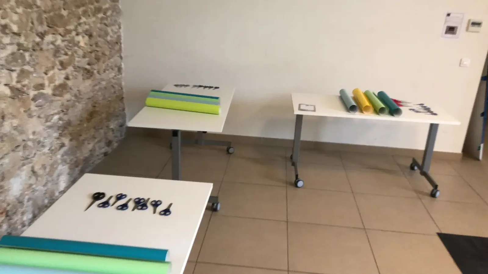 Tables préparées avec rouleaux de vinyle adhésif et ciseaux pour une fresque artistique à Paris.