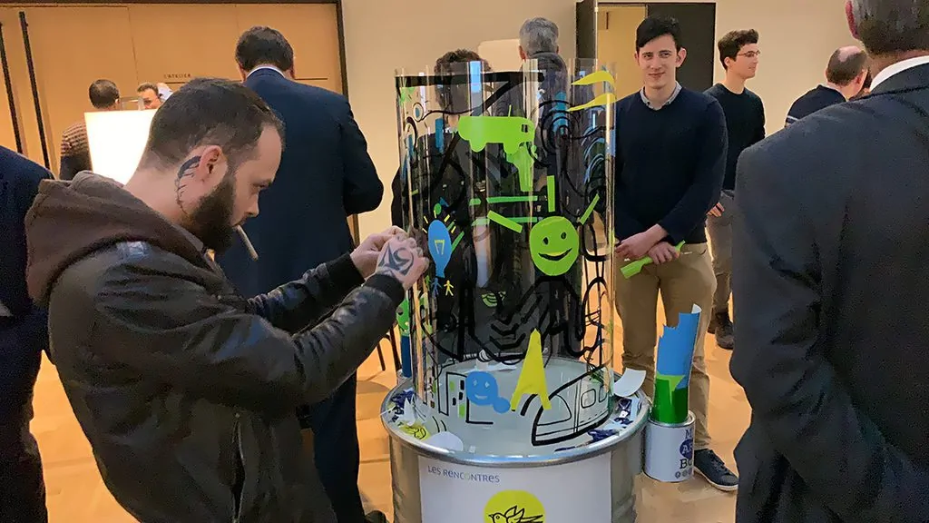 Une participante applique avec précision un sticker découpé sur une fresque collective transparente.