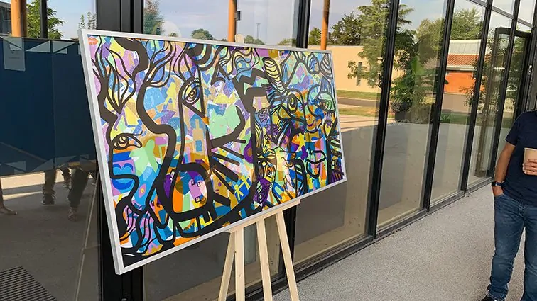 Une fresque colorée encadrée dans un support sur mesure posé sur un chevalet lors d'un séminaire.
