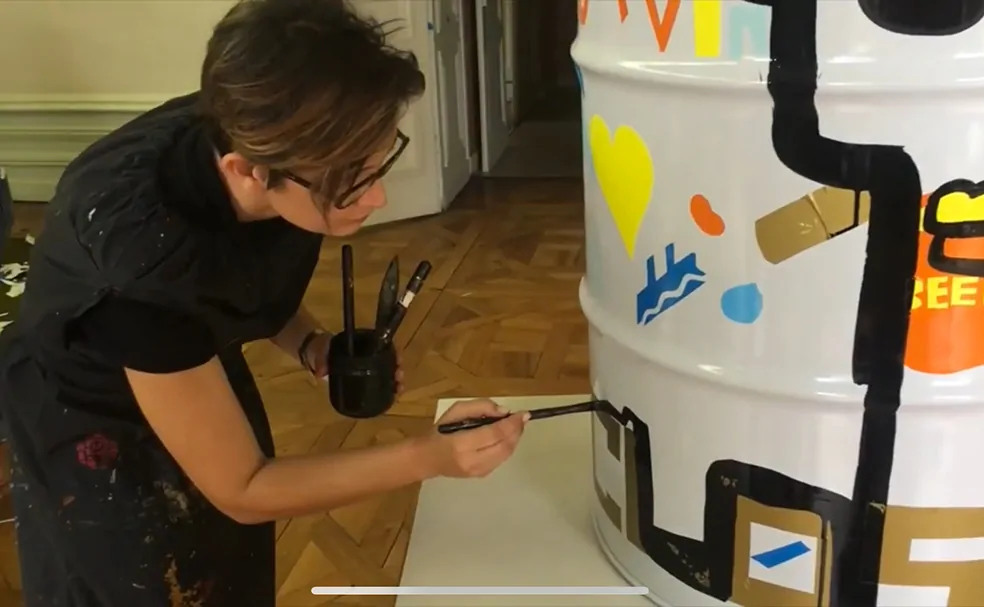 Une artiste peint des motifs colorés sur des fûts métalliques lors d'un atelier créatif en entreprise.