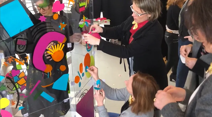Participants en train de peindre ensemble sur une grande paroi transparente en plexiglas lors d'un événement.