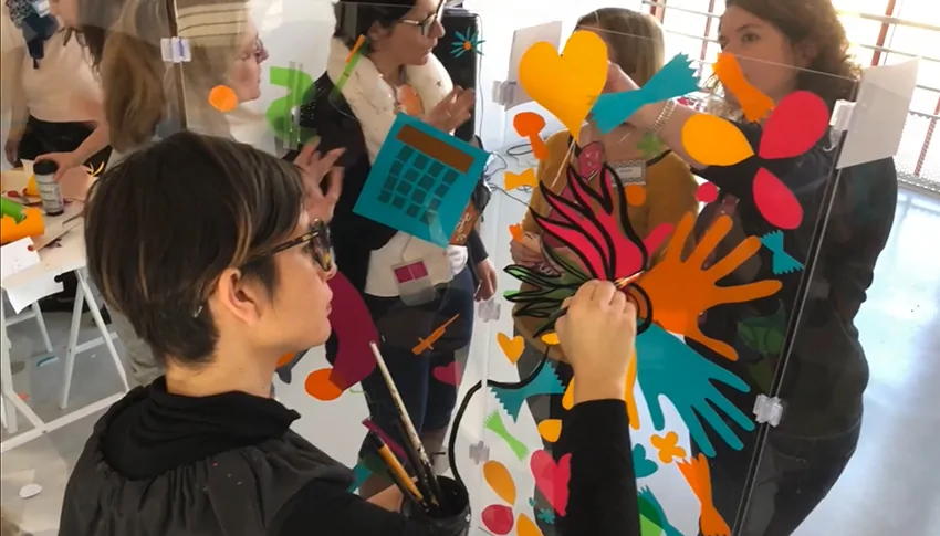 Participants créant une œuvre collective sur un support en plexiglas transparent lors d'un événement en Bretagne.