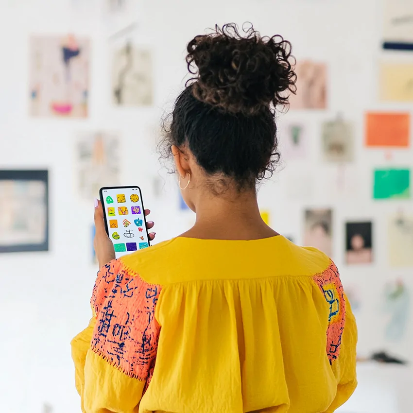 La fresque de mon identité en train d'être composée des dessins d'enfants sur l'application POSITIVE par une femme orientale aux cheveux bouclés et qui porte un chemisier jaune