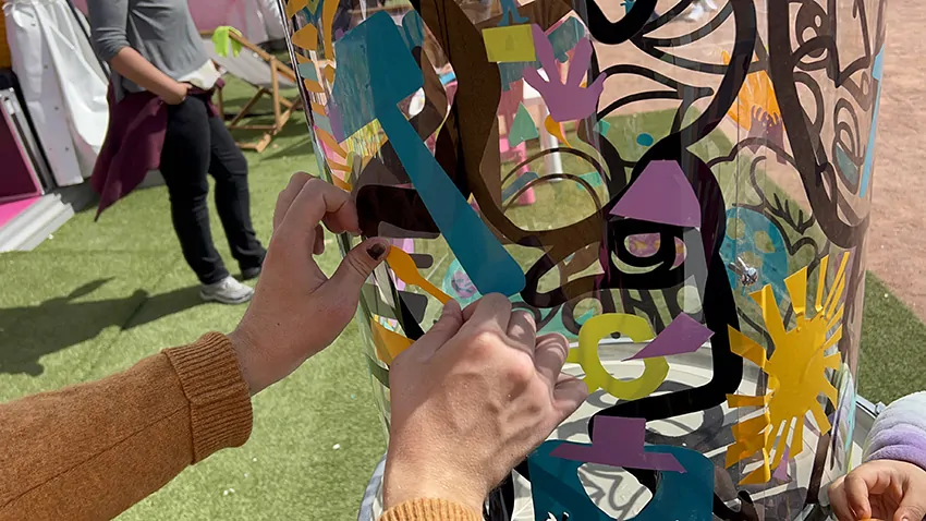 Une participante colle son idée découpée une forme de petite cuillère dans le vinyle orange avec des ciseaux de réemploi pour une oeuvre collective sans peinture Totem plexi My-art-box rse écoresponsable