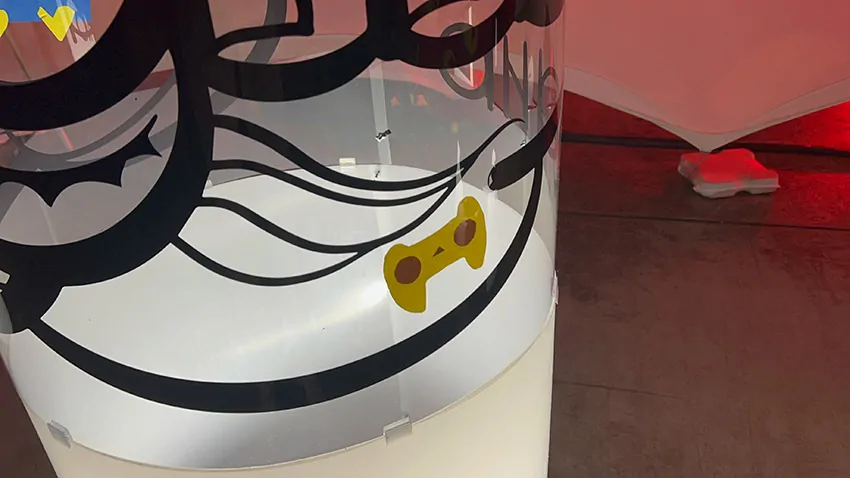 Une poignée de jeu Playstation découpée dans le vinyle écoresponsable sur la fresque des jouets My Art Box sous forme de totem tube plexi en cours de création lors d'un anniversaire d'entreprise à Lons le Saunier