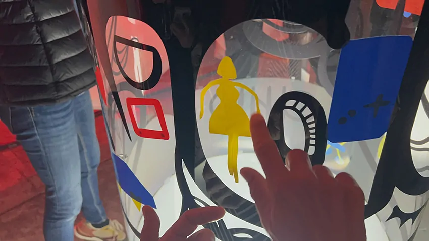 Un joli symbole de poupée jaune découpée dans le vinyle écoresponsable sur la fresque des jouets My Art Box sous forme de totem tube plexi en cours de création lors d'un anniversaire d'entreprise à Lons le Saunier