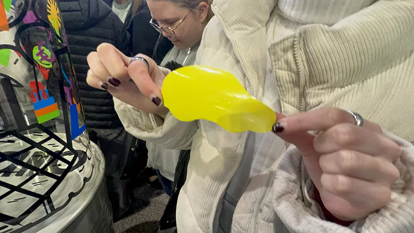 Une voiture jaune découpée dans du vinyle que la participante colle ensuite sur fresque plexi éco-responsable My Art Box en animation de stand pour scolaires à Grenoble