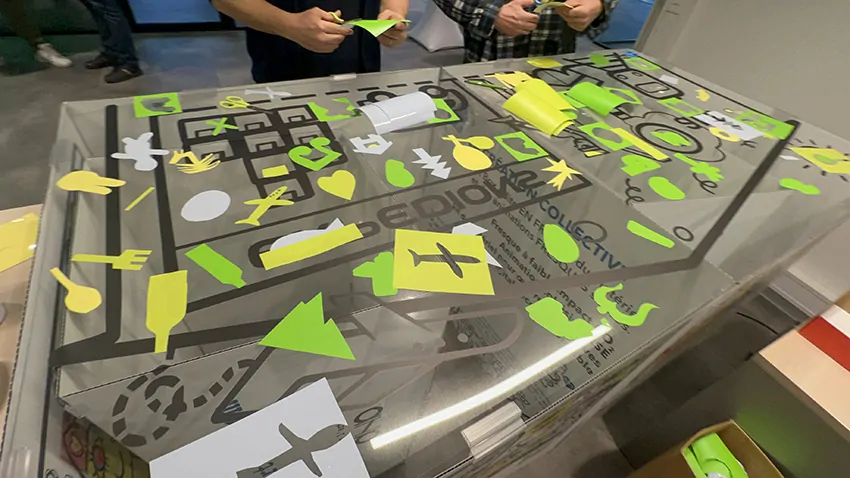 La fresque des passions et des participants devant le plexi en train de découper du vinyle de couleur adhésif à Genève