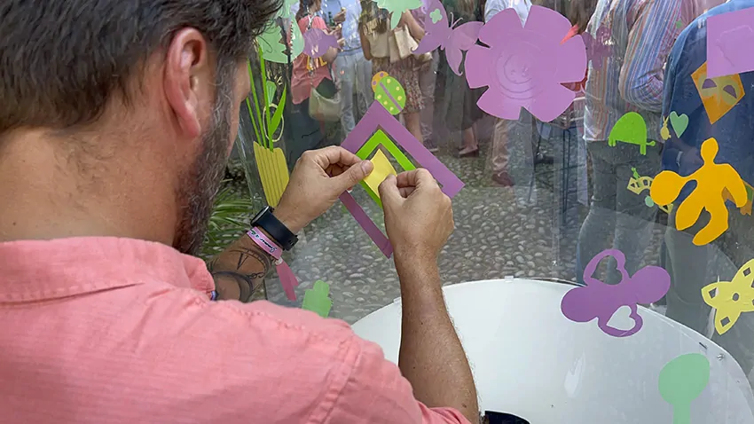 Un participant à l'animation originale fresque en garden party à Genève en Suisse colle son idée découpée dans du vinyle de couleur sur le Tube plexi de aNa artiste