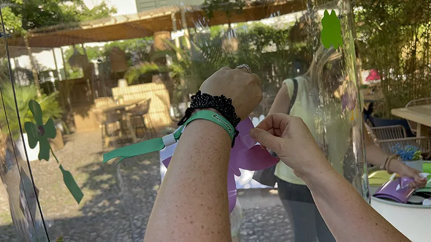 Un symbole de papillon en train d'être collé sur le plexi de la fresque en garden party à Genève en Suisse par une participante à l'animation My Art Box coachée par Christophe Chazot