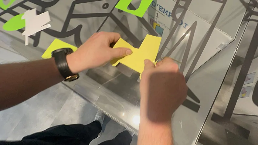 Un participant colle son idée découpée dans du vinyle de couleur sur la fresque des passions en plexiglas à Genève au milieu de 100 convives