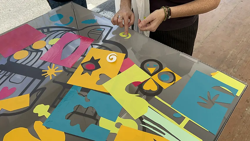 Une participante colle son idée découpée dans du vinyle sur la fresque du tri My Art Box pendant l'animation à Albi