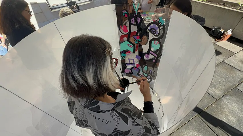 ana artiste concentrée en train de peindre dans son tube plexi sobre et éco-responsable en team building secteur de la petite enfance à Genève entourée des participantes à l’extérieur du cylindre