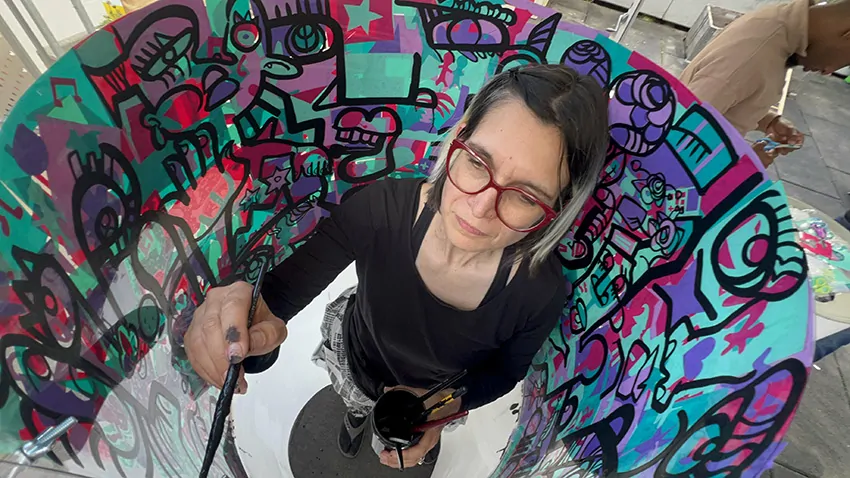 ana artiste termine de peindre sa fresque RSE dans son tube plexi rse en team building secteur de la petite enfance à Genève