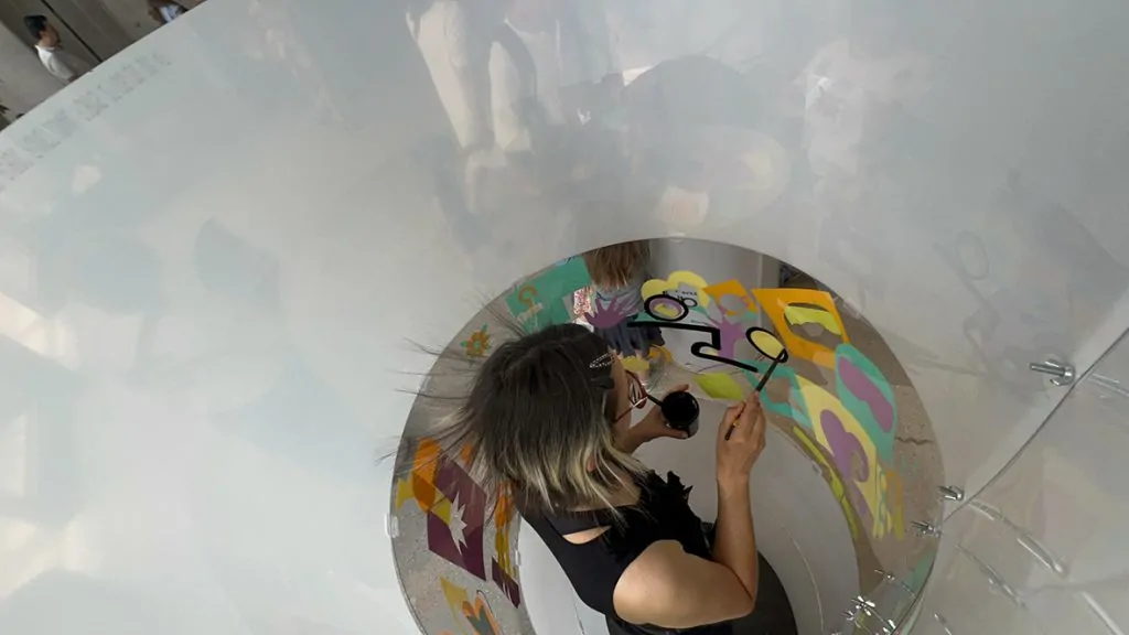 ana artiste en train de peindre dans son tube en plexiglas lors de l'animation fresque éco-responsable à Genève organisée par My Art Box