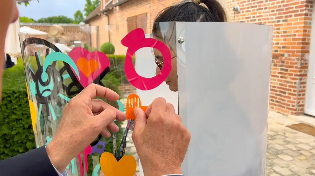 Un participant l'animation fresque pour mariage à Orleans colle un sticker découpé orange sur le plexiglas de aNa artiste