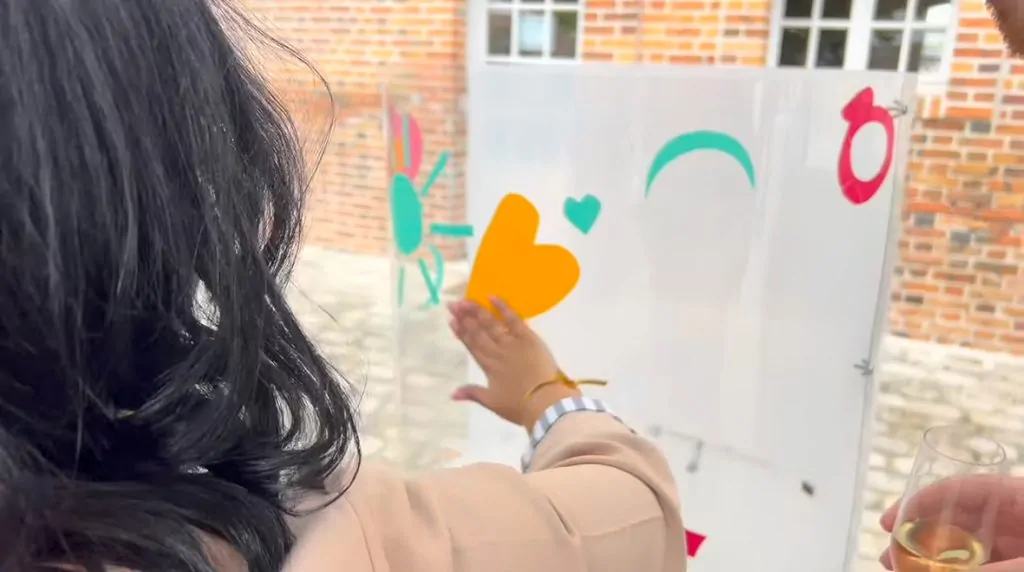 Une participante l'animation fresque pour mariage à Orleans colle un sticker découpé en forme de coeur orange sur le plexiglas de aNa artiste